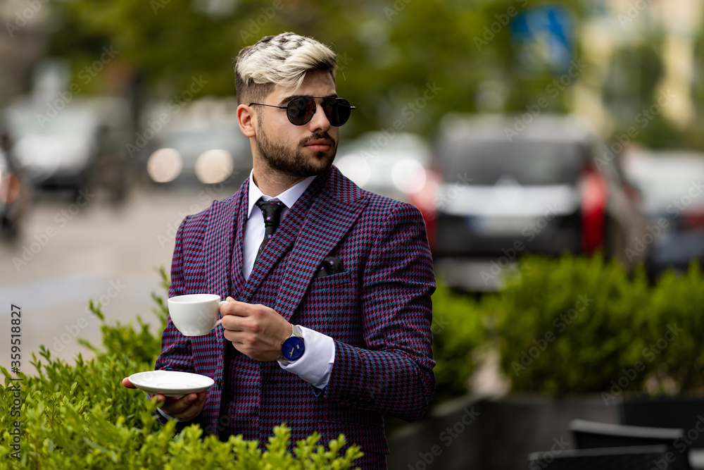 Fototapeta premium photo of man at the cafe wearing on violet luxery three-piece suit drinking coffee or tea from cup