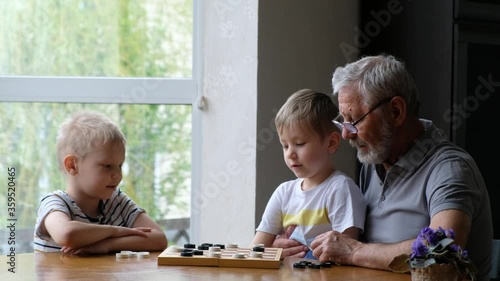 Kids play checkers with grandfather at home, senior positive man