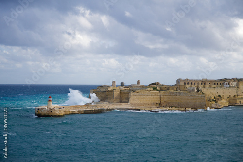 VALLETTA, MALTA - DEC 31st, 2019: View from Fort St Elmo on to the Ricasoli Grand Harbour East Breakwater and red lighthouse during strong waves © miles_around