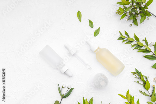 Retinols serum and hyaluronic acid bottle on white concrete with green leaves branches. Organic healing cosmetics. Eco skin care. Beauty treatment