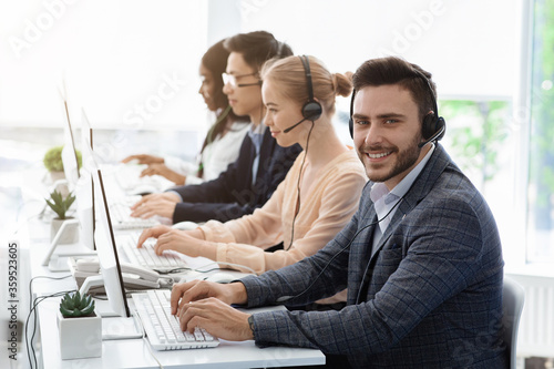 Team of customer service agents with headsets working at computers in office, empty space
