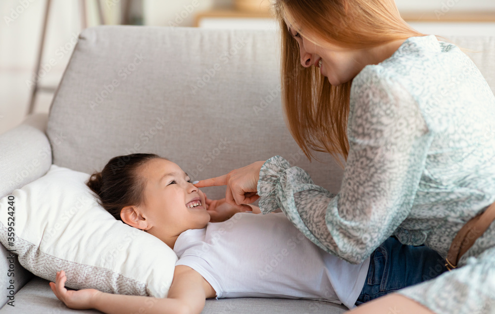 Happy Mother Touching Daughter's Nose Laughing Sitting On Sofa Indoor Happy Mother Touching Daughter's Nose Laughing Sitting On Sofa Indoor