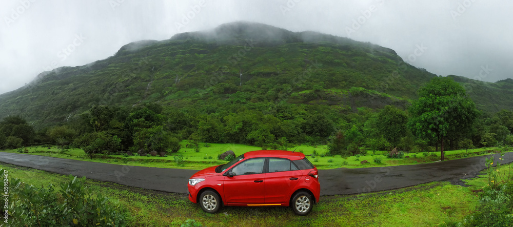 Red car parked on the road beside a mountain on a rainy day
