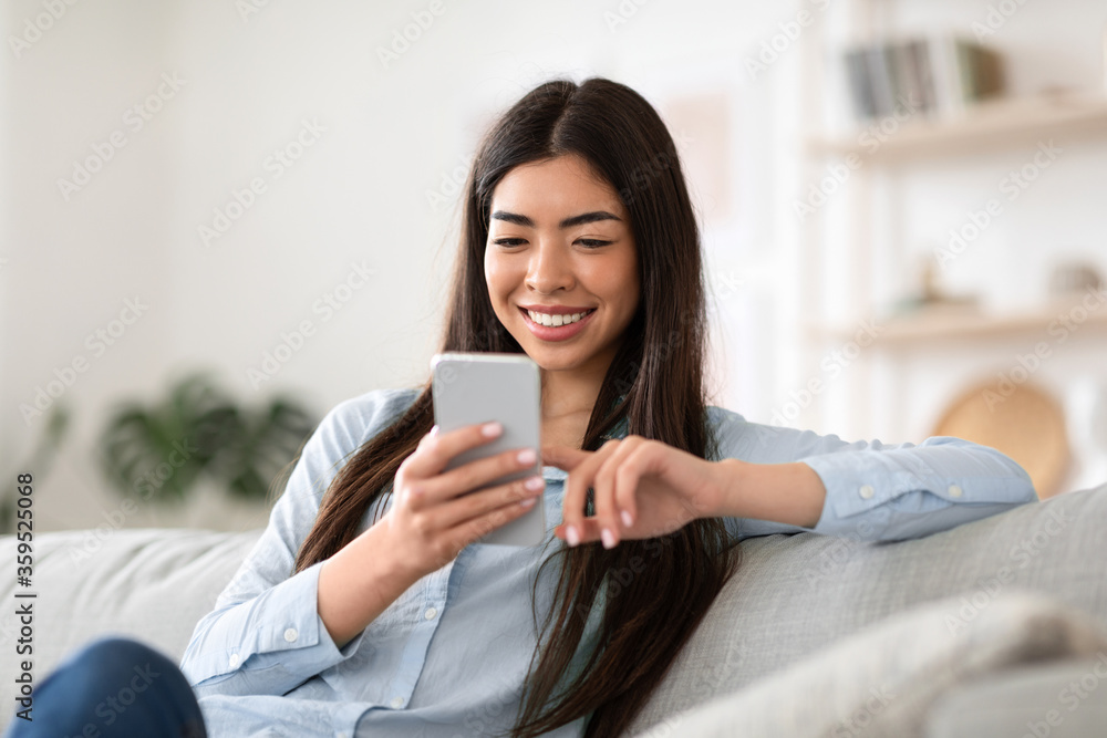 Weekend Pastime. Smiling asian girl browsing internet on smartphone at home Weekend Pastime. Smiling asian girl browsing internet on smartphone at home