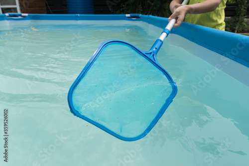 hands hold stick with big blue net and clean water in swimming pool from dust and insects. Maintenance and keeping pool clean. photo