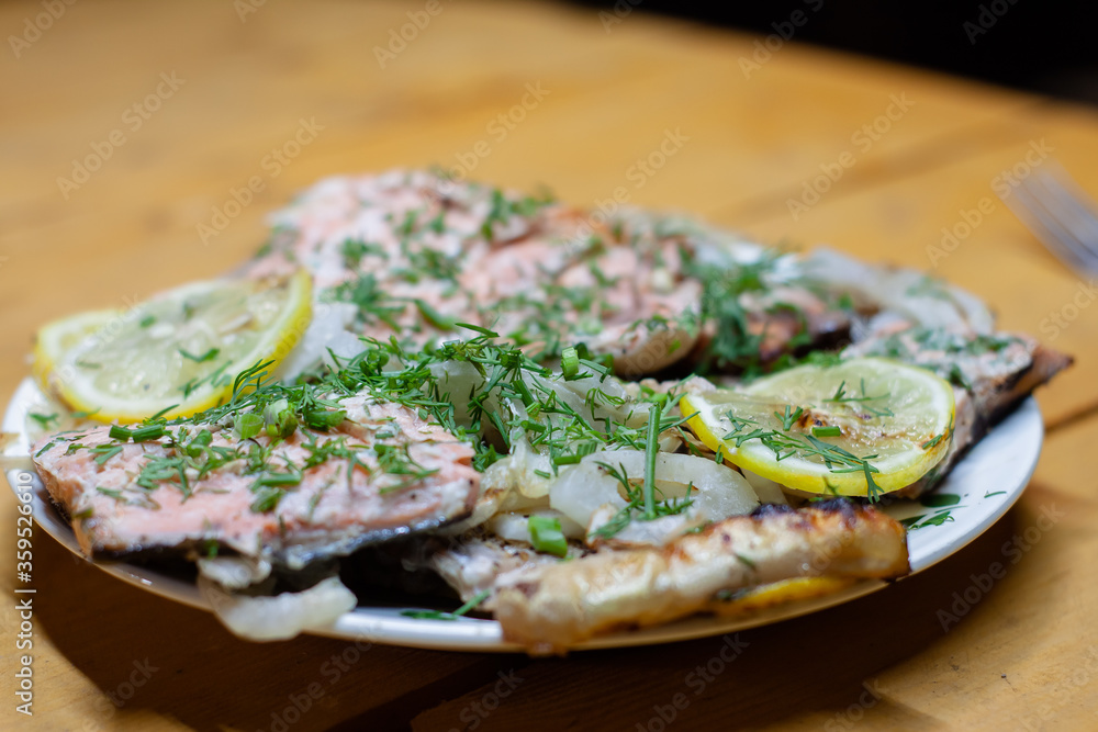 pieces of red fish with lemon on a plate decorated with greens. cooking on the grill. pieces of red fish with lemon on a plate decorated with greens. cooking on the grill.