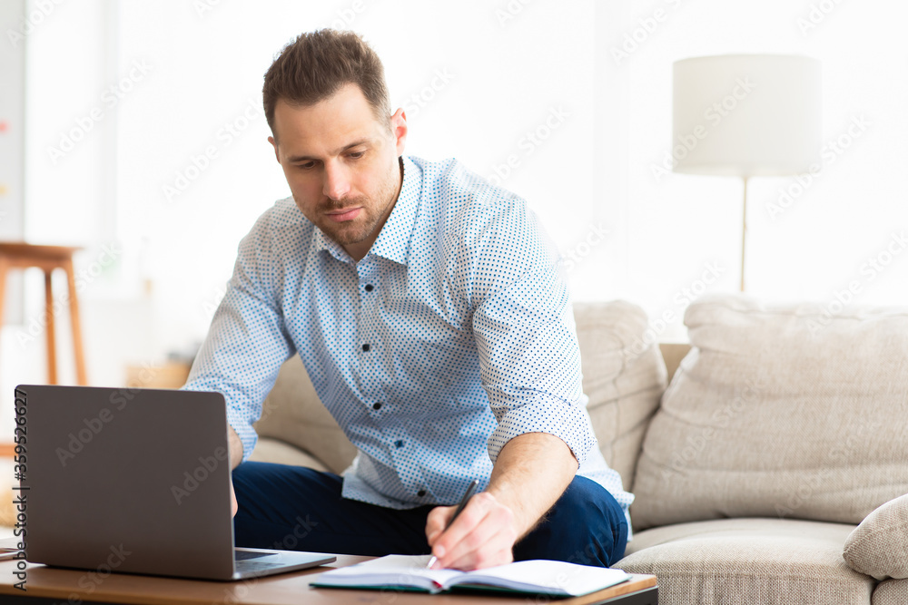 Focused man using laptop at home and writing notes Focused man using laptop at home and writing notes