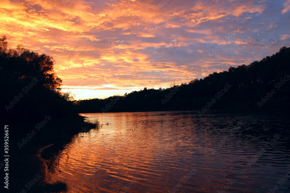 Fototapeta premium Beautiful blazing sunset landscape above river and orange sky in evening