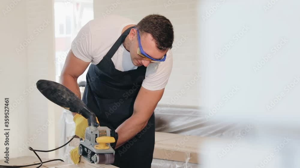 A worker polishes a pine board with a grinding tool. A man holds a power tool for grinding and polishing the surface of a wooden board. A wood craftsman works with his own hands. A worker polishes a pine board with a grinding tool. A man holds a power tool for grinding and polishing the surface of a wooden board. A wood craftsman works with his own hands.