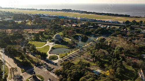 Aerial view of the planetary round dome building in the middle of a public park with green grass, trees, and a little lake around, during the sunset in Buenos Aires, Argentina.