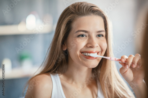 Young girl with beautiful smile brushing her teeth in front of mirror at bathroom