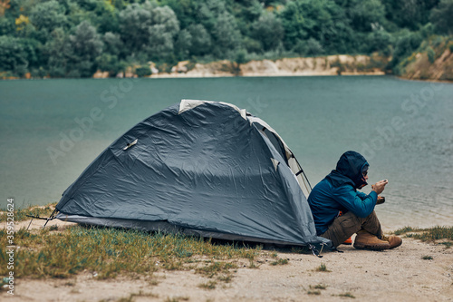 Man sitting on shore by the lake and eating his lunch on camping trip.