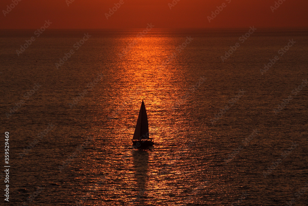 Fototapeta premium Żaglówka na morzu na tle zachodzącego słońca.
