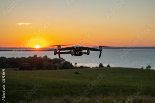 Quadrocopter in flight against the background of the river at the setting sun. The drone's tail lights are on. Copy space.