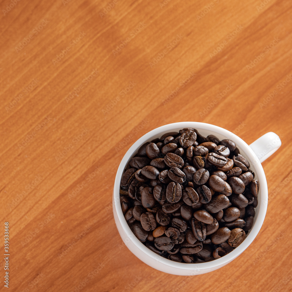 Fototapeta premium White Cup with dark brown coffee beans on the background of the table.