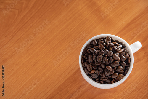White Cup with dark brown coffee beans on the background of the table.