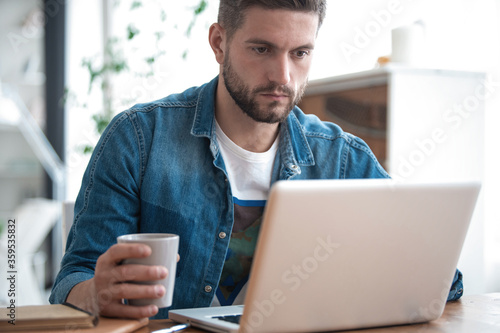 Handsome modern man designer working on laptop online, using internet at home