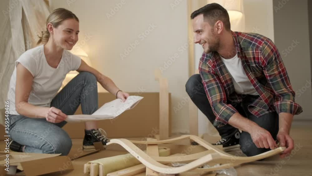 Young adults moving in new home. Couple moving in assembling chair furniture. Young interracial couple in new home. repair, renovation and people concept Young adults moving in new home. Couple moving in assembling chair furniture. Young interracial couple in new home. repair, renovation and people concept