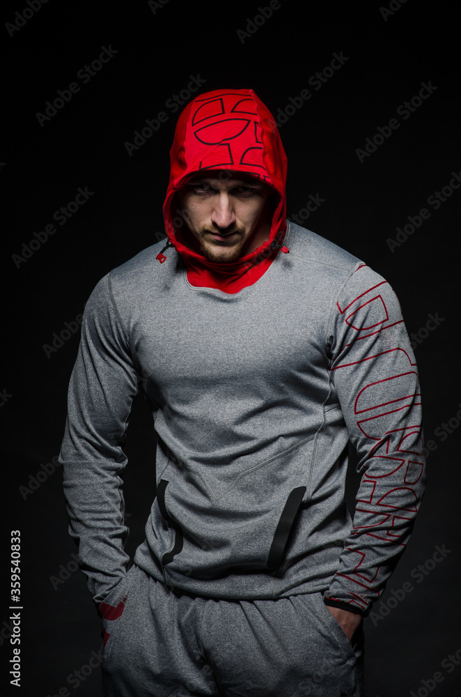 A sporty guy stands in the Studio against a dark background in a hood. Sports, beauty