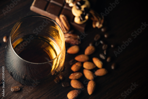 Cognac glass with brandy, chocolate, nuts, amber flare of cognac on a black background.