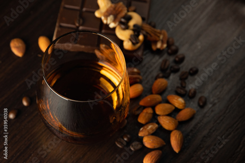 Cognac glass with brandy, chocolate, nuts, amber flare of cognac on a black background.