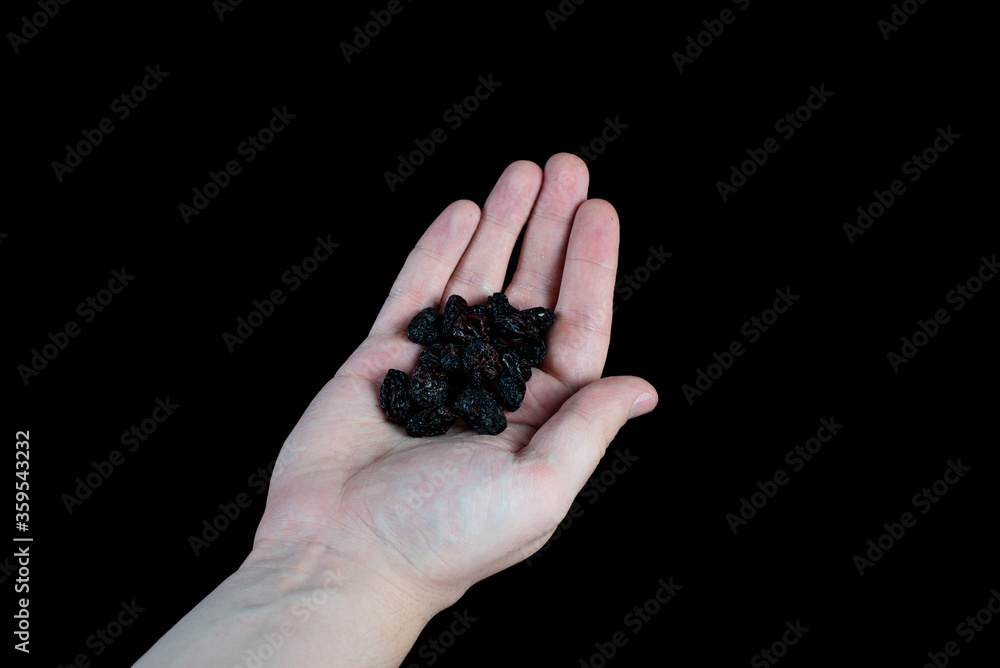handful of black raisins on the palm on a black background handful of black raisins on the palm on a black background