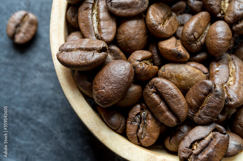 extreme close-up of a wooden bowl filled with roasted coffee bean on a dark slate background. horizontal format with copy space for text photo