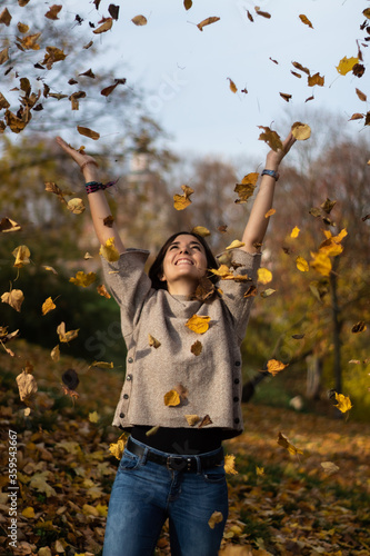 Attractive young female throwing leaves to the air on a cold fall´s morning 
