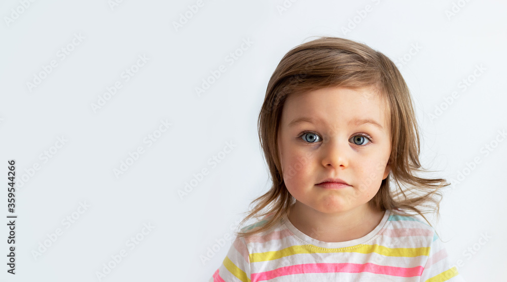 Neutral expression, sad looking child toddler girl wearing striped t-shirt against neutral background Neutral expression, sad looking child toddler girl wearing striped t-shirt against neutral background