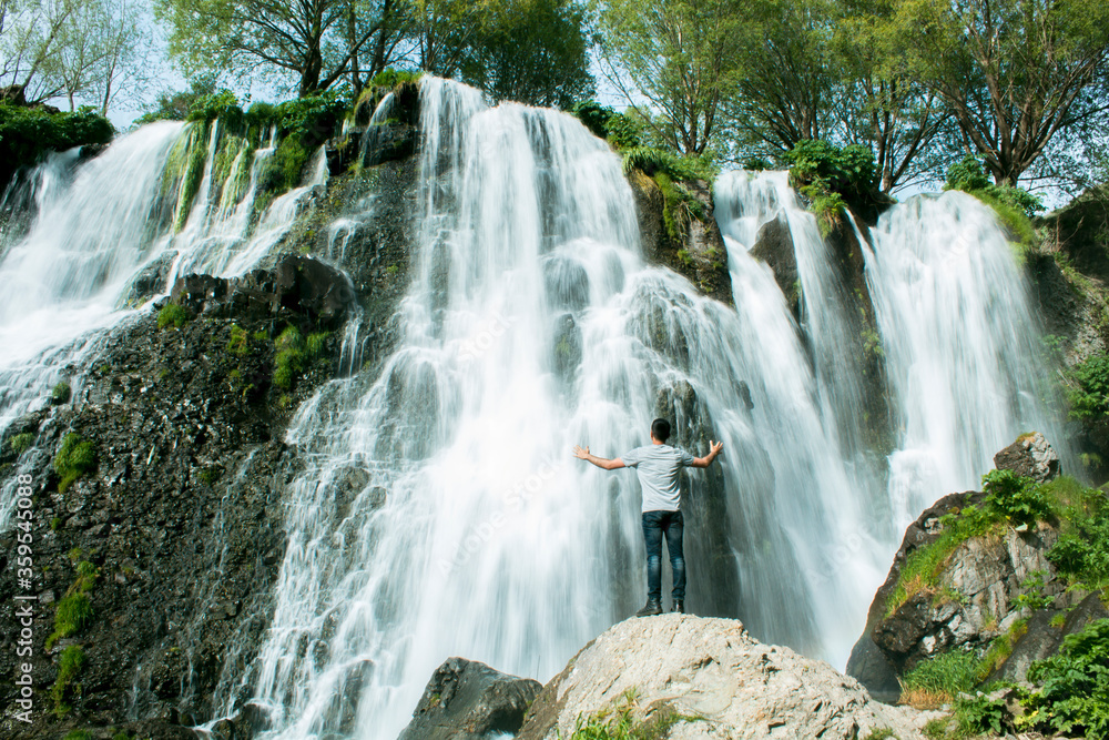 Fototapeta premium A man with his hands open stands by a waterfall