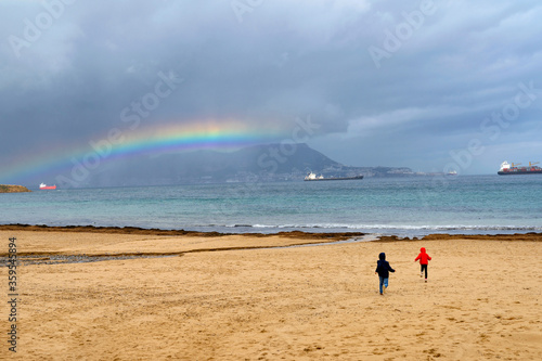 Beautiful view of Gibraltar Peninsula. Children running towards the rainbow. Impressive ships traveling through the Bay of Algeciras, Andalusia, Southern Spain.