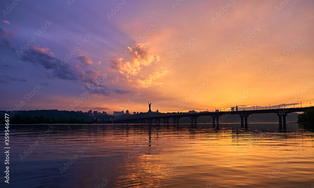 Orange blue sunset on the Dnieper river in Kyiv. Panorama of the bridge. Clouds in the sky.
