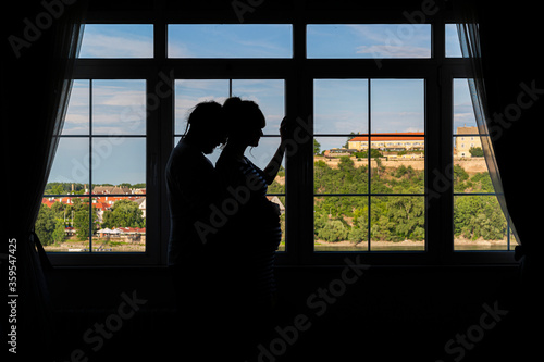 Silhouette of a young pregnant couple by the window.