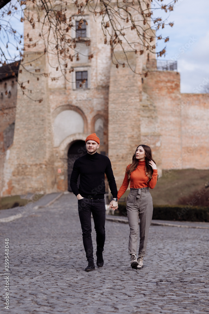 Beautiful Tourist Couple In Love Walking On Street Together. Happy Young Man And Smiling Woman Walking Around Old Town Streets, Looking At Architecture. Travel Concept.