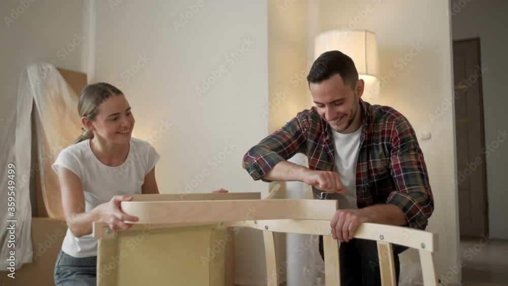 Young adults moving in new home. Couple moving in assembling chair furniture. Young interracial couple in new home. repair, renovation and people concept Young adults moving in new home. Couple moving in assembling chair furniture. Young interracial couple in new home. repair, renovation and people concept