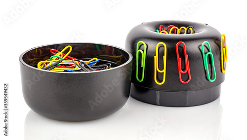 Disassembled on two parts cylindrical black plastic magnetic holder with colored paper clips isolated on white background