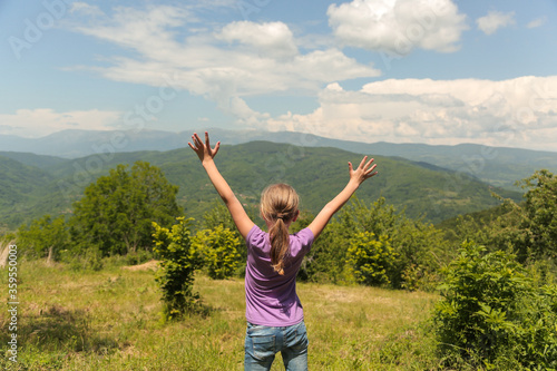 Happy little girl enjoying nature on grass meadow on top of mountain . Freedom, children tourism concept. 