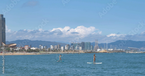 Photography Two girls doing paddle surf in the Barcelona sea with the Barcelona skyline