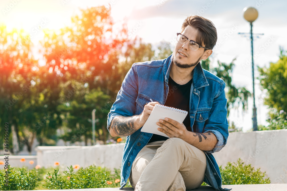 Obraz premium Young handsome freelancer writing in notebook outdoors. Outdoor work concept.
