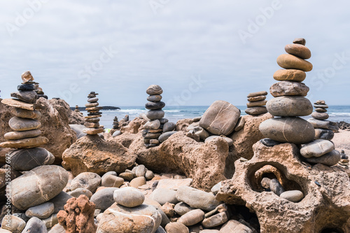 Pebbles heaped and balanced in a tower on top of mineral rocks in cityscape - Zen image of tranquility at Farol beach in Milfontes, Vicentine Coast Natural Park PORTUGAL