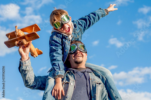 Dad and son wearing pilot glasses imitate pilots, holding a wooden plane in their hands on a white background. The end of the epidemic coronavirus covid-19. Opening borders. Summer travel. Parenting