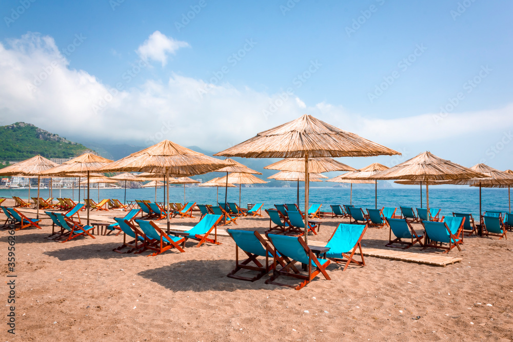 Thatched beach umbrellas and stylish sun loungers on Becici beach in Budva. Beach season on the Adriatic