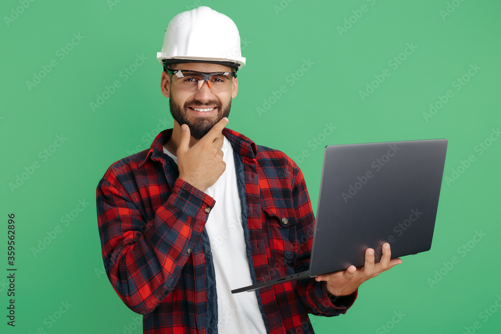 Handsome bearded engineer or constructor man in casual outfit with computer over green background. Handsome bearded engineer or constructor man in casual outfit with computer over green background.