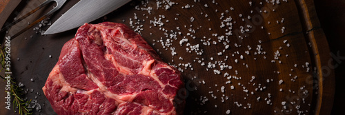 Top view of raw Chuck Eye beef steak seasoned with coarse salt and rosemary, on a dark wooden textured surface, with space for writing.