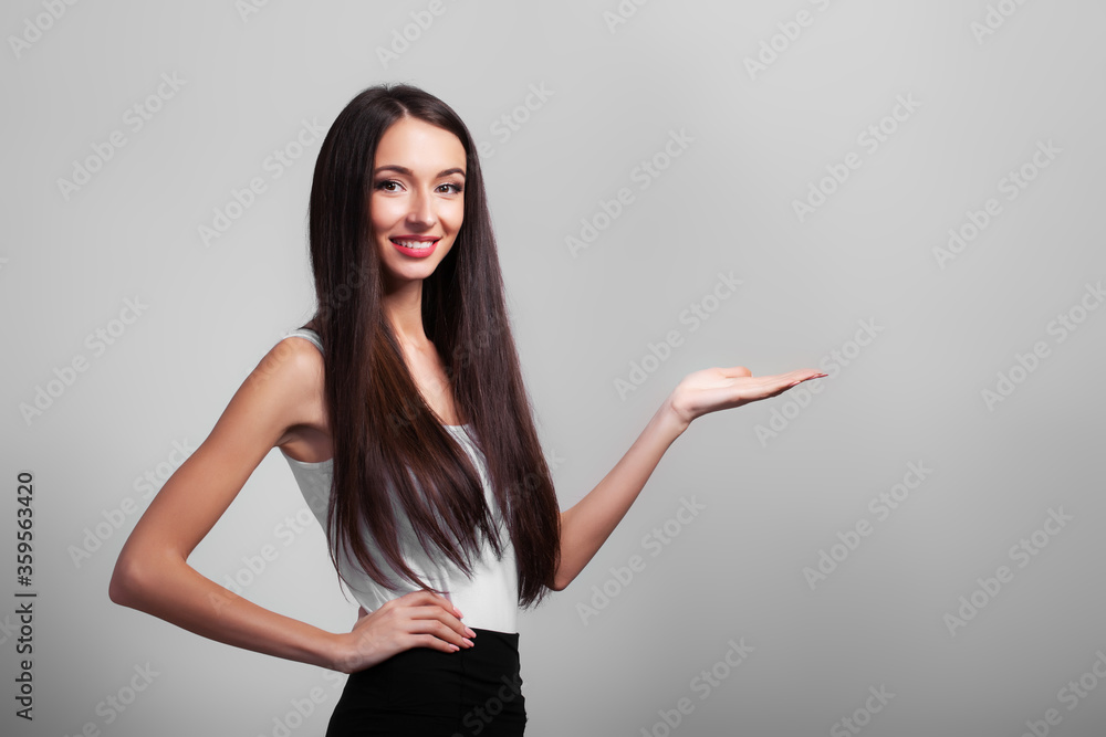 Cute business woman shows your product with her hand on gray background. Cute business woman shows your product with her hand on gray background.