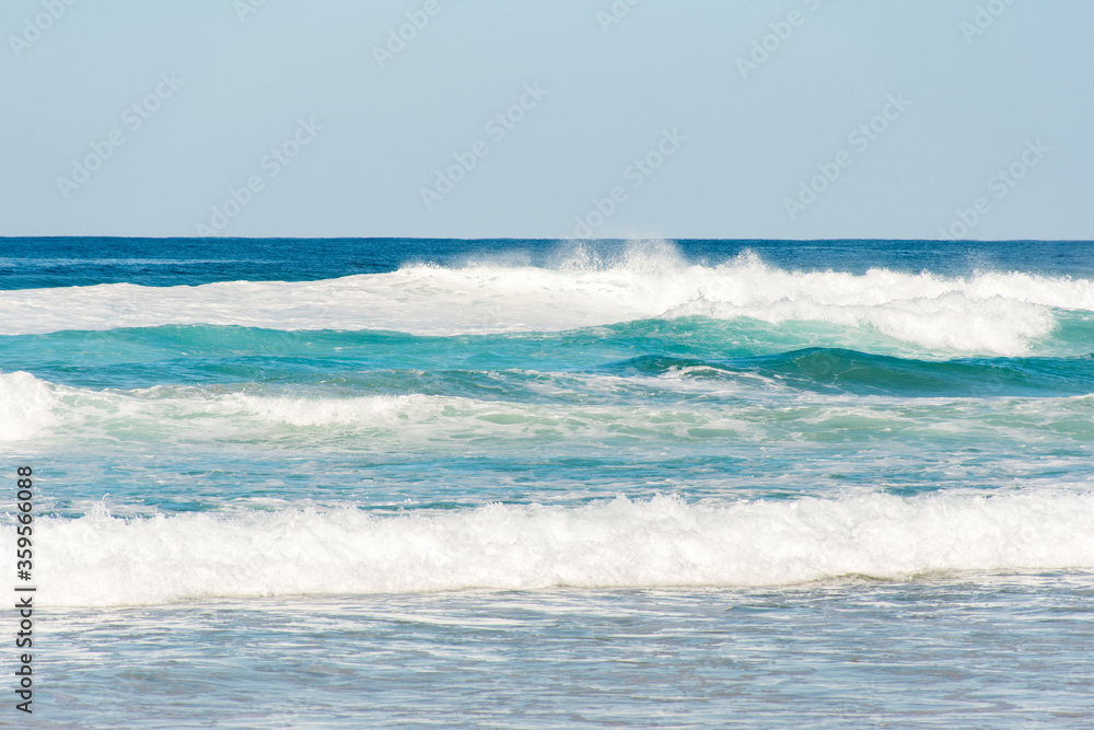 Ocean waves with white foam splashes on a bright sunny day. Background with copy space
