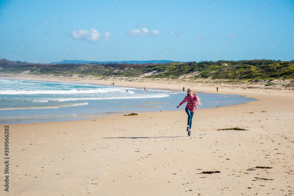 A girl skipping on a scenic beauriful sandy Bendalong Beach on sunny winter day. Bendalong, NSW, Australia.