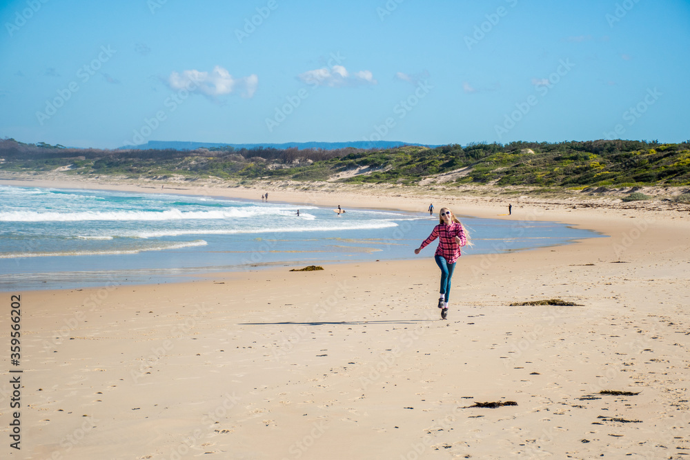 A girl skipping on a scenic beauriful sandy Bendalong Beach on sunny winter day. Bendalong, NSW, Australia. A girl skipping on a scenic beauriful sandy Bendalong Beach on sunny winter day. Bendalong, NSW, Australia.