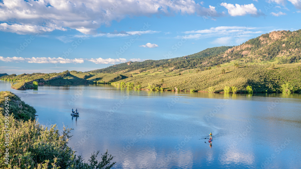 summer morning on  Horsetooth Reservoir at foothills of Rocky Mountains in northern Colorado with a fishing boat and a stand up paddler, popular recreation destination in Fort Collins area