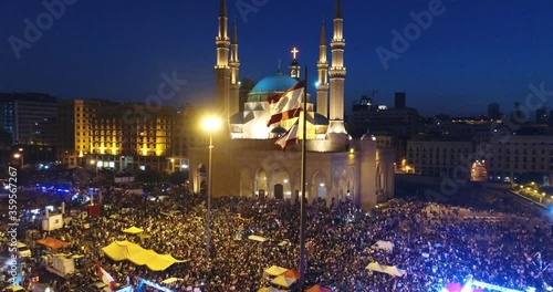 Beirut, Lebanon 2019 : night drone shot in Martyr square, jib up with Lebanese flag in foreground, church and mosque in background and people revolting against government  during Lebanese revolution photo